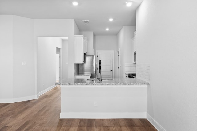 kitchen with a peninsula, light stone counters, white cabinets, and a sink