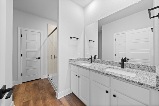 bathroom with double vanity, wood finished floors, a sink, and a shower stall