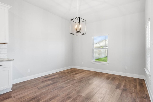 unfurnished dining area with an inviting chandelier, wood finished floors, and baseboards