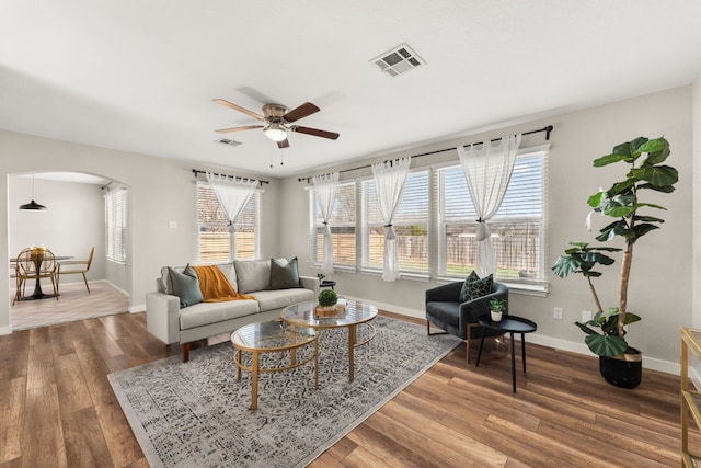 living area featuring arched walkways, visible vents, baseboards, and wood finished floors