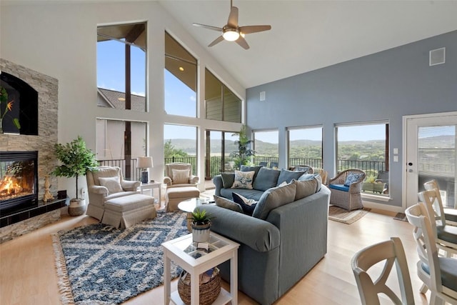 living room featuring a fireplace, lofted ceiling, visible vents, a ceiling fan, and light wood-type flooring