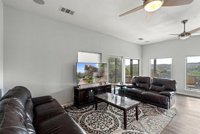 living area with a textured ceiling, a wealth of natural light, wood finished floors, and visible vents