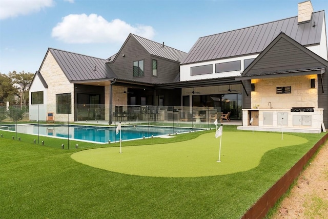 rear view of house with ceiling fan, metal roof, stone siding, a fenced in pool, and a standing seam roof