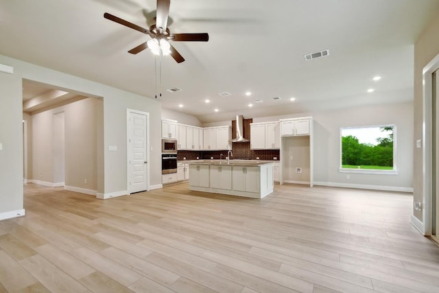 kitchen featuring open floor plan, stainless steel microwave, wall chimney range hood, and oven