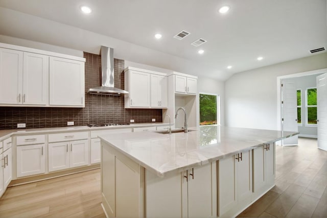 kitchen featuring visible vents, stainless steel gas cooktop, wall chimney exhaust hood, tasteful backsplash, and a sink