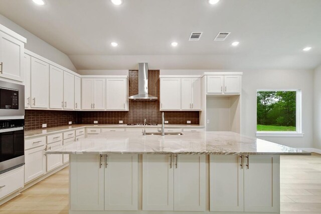 kitchen with wall chimney range hood, stainless steel appliances, visible vents, and a large island with sink
