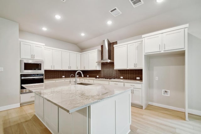 kitchen featuring oven, a sink, wall chimney exhaust hood, stainless steel microwave, and visible vents