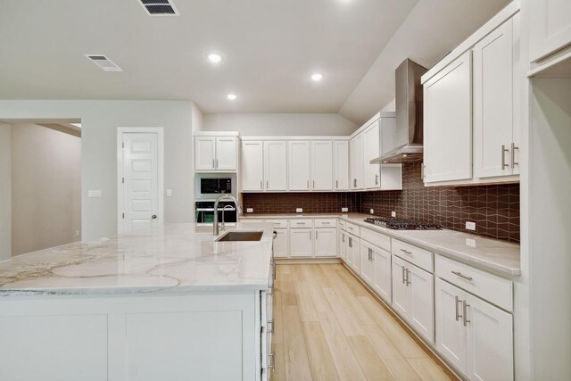kitchen featuring a kitchen island with sink, built in microwave, wall chimney exhaust hood, white cabinetry, and tasteful backsplash