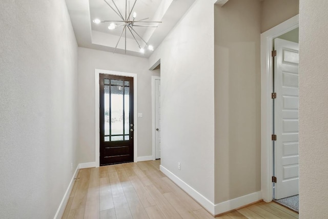 foyer with baseboards, a tray ceiling, light wood-type flooring, and a chandelier
