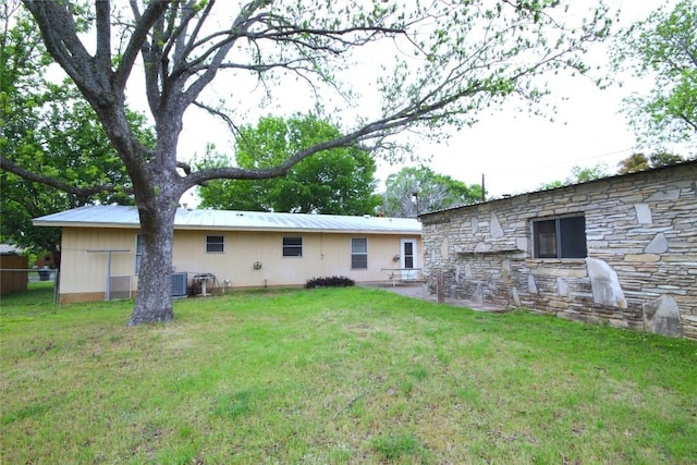 back of house featuring stone siding, a lawn, and central air condition unit