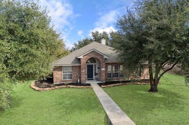 view of front of house featuring brick siding, a chimney, a front yard, and a shingled roof