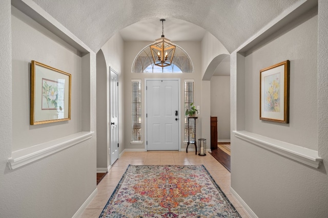 foyer entrance with baseboards, arched walkways, a textured ceiling, a notable chandelier, and light tile patterned flooring