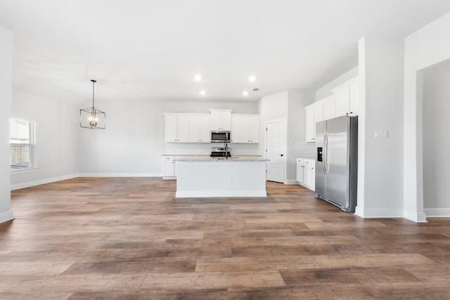 kitchen featuring an island with sink, open floor plan, stainless steel appliances, white cabinetry, and pendant lighting