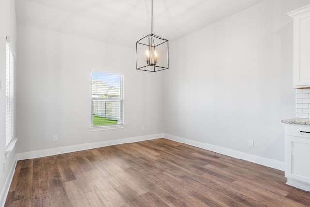 unfurnished dining area with a notable chandelier, baseboards, and wood finished floors