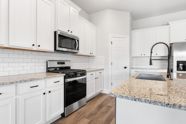 kitchen with dark wood-style flooring, a sink, white cabinetry, appliances with stainless steel finishes, and light stone countertops