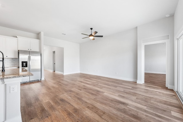 unfurnished living room featuring light wood-style flooring, baseboards, and ceiling fan