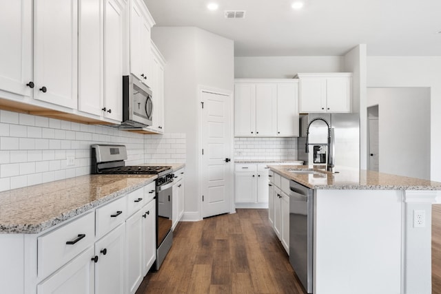 kitchen with appliances with stainless steel finishes, a center island with sink, and white cabinets