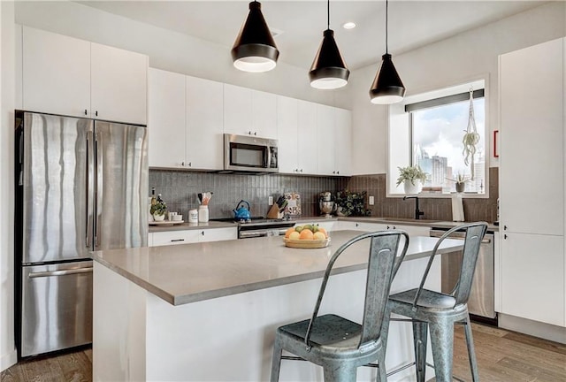 kitchen with wood finished floors, a sink, white cabinets, appliances with stainless steel finishes, and a center island