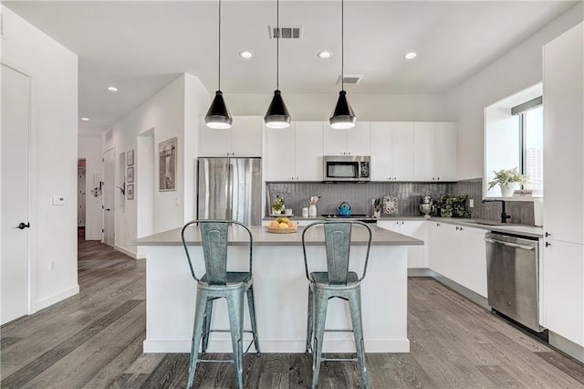 800 Embassy Dr Unit 319, Austin, TX 78702 - kitchen featuring appliances with stainless steel finishes, a kitchen island, wood finished floors, backsplash, and a breakfast bar