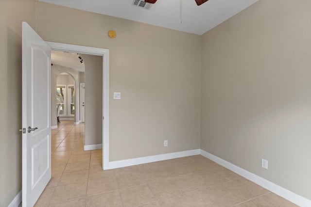 empty room with arched walkways, light tile patterned floors, visible vents, ceiling fan, and baseboards