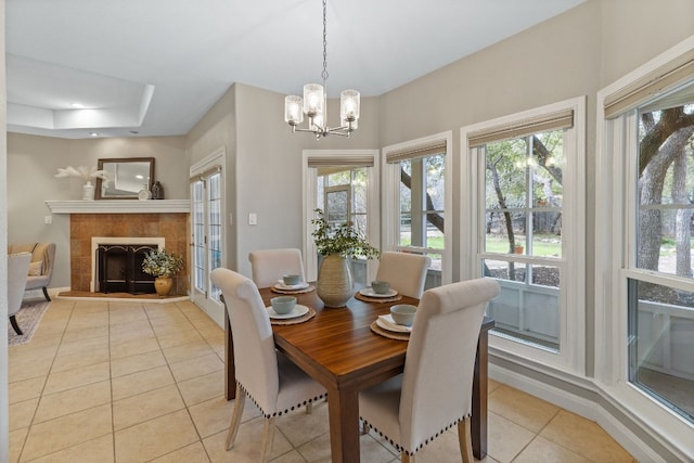 dining area with light tile patterned floors, a chandelier, a fireplace, baseboards, and a tray ceiling