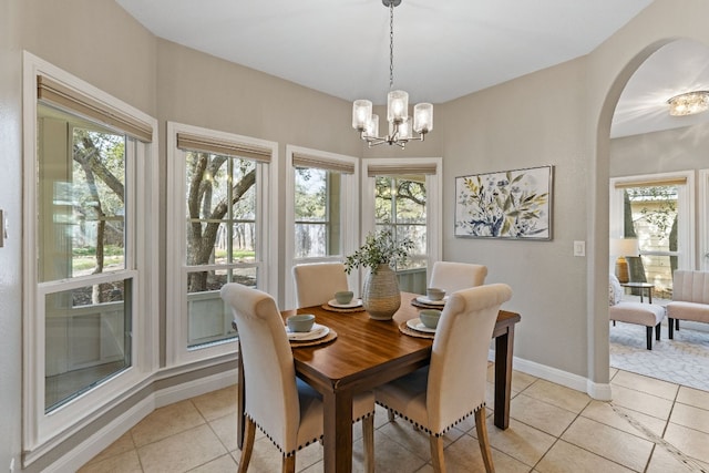 dining space featuring an inviting chandelier, baseboards, arched walkways, and light tile patterned flooring