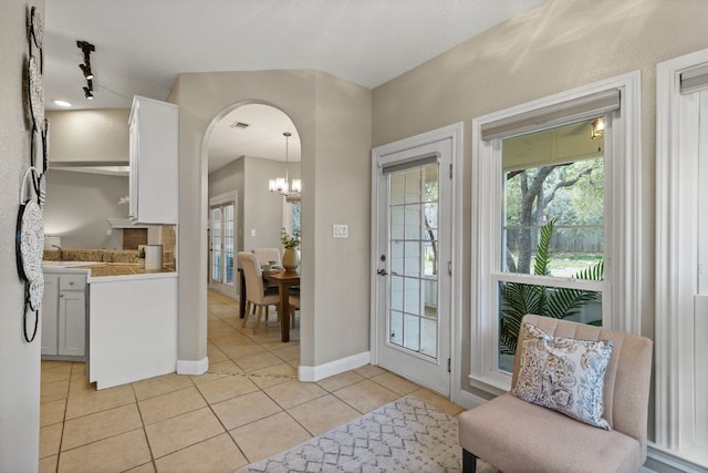 doorway to outside with arched walkways, light tile patterned flooring, baseboards, and an inviting chandelier