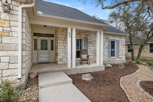 property entrance featuring stone siding, a porch, and roof with shingles