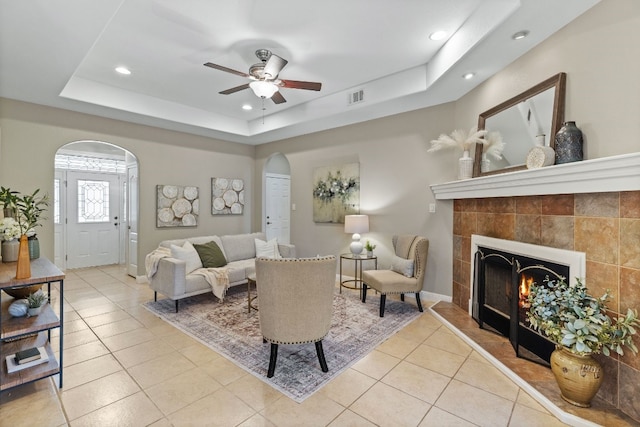 living room featuring light tile patterned floors, visible vents, arched walkways, a raised ceiling, and a tiled fireplace