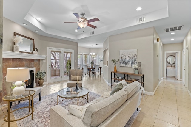 living area featuring light tile patterned floors, a tiled fireplace, a raised ceiling, and visible vents