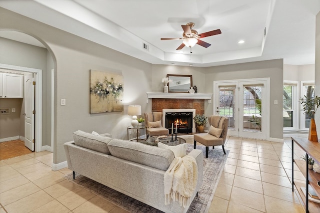 living area featuring arched walkways, light tile patterned flooring, a fireplace, visible vents, and a tray ceiling