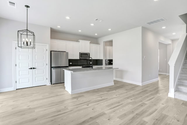 kitchen with appliances with stainless steel finishes, white cabinets, visible vents, and a center island with sink