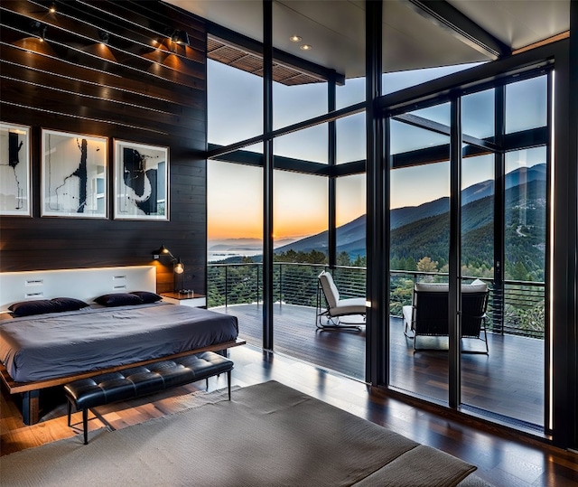 bedroom featuring access to exterior, expansive windows, a mountain view, wooden walls, and wood finished floors