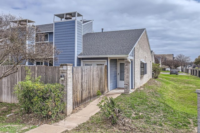 view of front facade featuring a shingled roof, a front yard, and fence