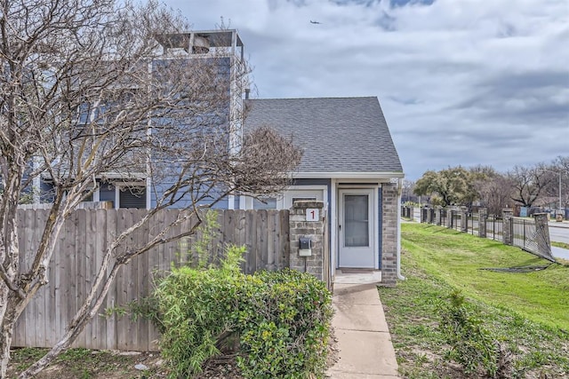 view of front facade with a front yard, fence, and roof with shingles