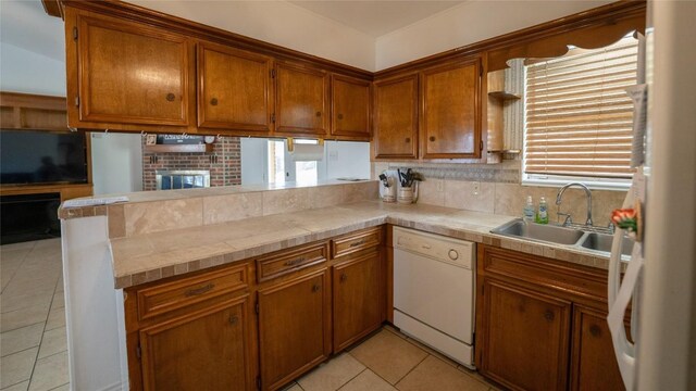 kitchen with brown cabinets, light countertops, a sink, dishwasher, and a peninsula