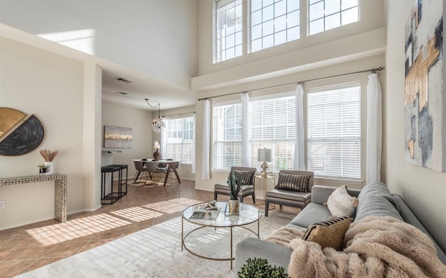 tiled living area featuring visible vents, plenty of natural light, a notable chandelier, and a towering ceiling