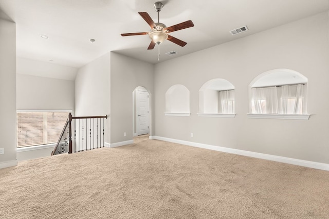 carpeted spare room featuring arched walkways, visible vents, and baseboards