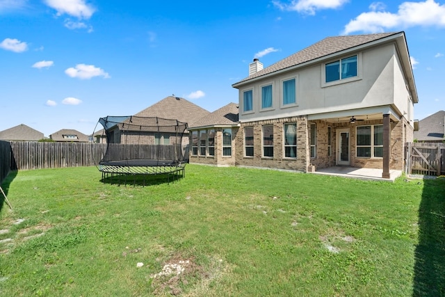 rear view of property featuring a patio, a fenced backyard, brick siding, a trampoline, and a chimney