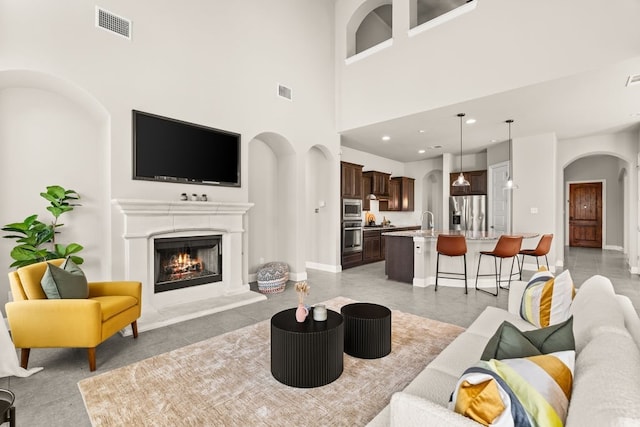 living room with a warm lit fireplace, arched walkways, visible vents, and recessed lighting