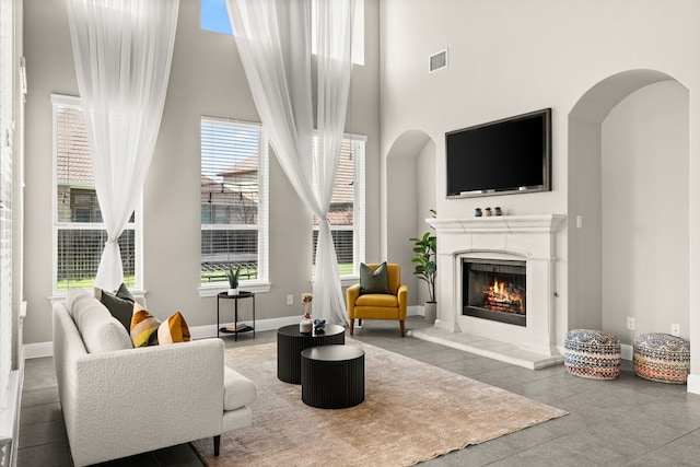 sitting room featuring a warm lit fireplace, visible vents, arched walkways, baseboards, and a towering ceiling