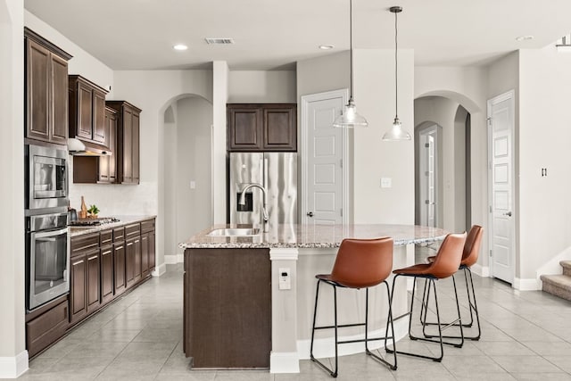 3809 Alpine Ridge Cv, Leander, TX 78641 - kitchen featuring appliances with stainless steel finishes, arched walkways, dark brown cabinetry, light tile patterned flooring, and recessed lighting