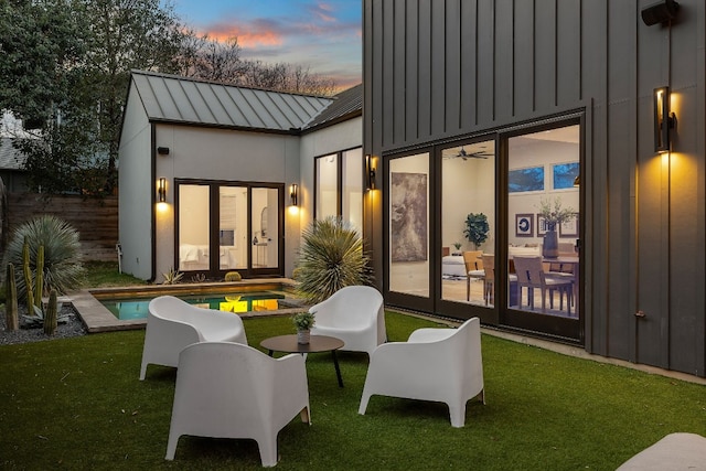 back of house at dusk featuring board and batten siding, a standing seam roof, an outdoor pool, and metal roof