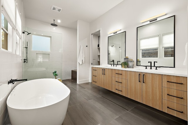 bathroom featuring tile walls, visible vents, a sink, a walk in shower, and a freestanding tub