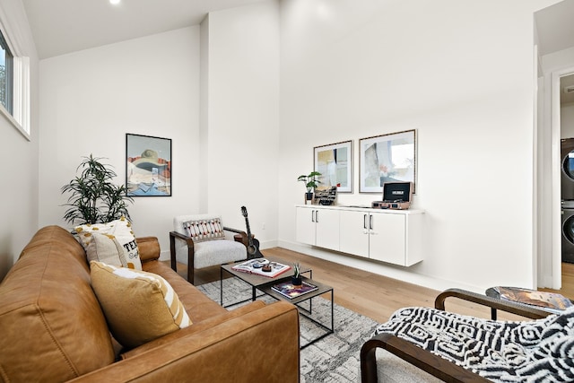 living room with a towering ceiling, light wood-style flooring, baseboards, and stacked washer and clothes dryer