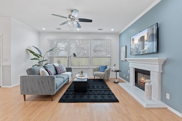 living room featuring a warm lit fireplace, light wood-style floors, baseboards, and ornamental molding