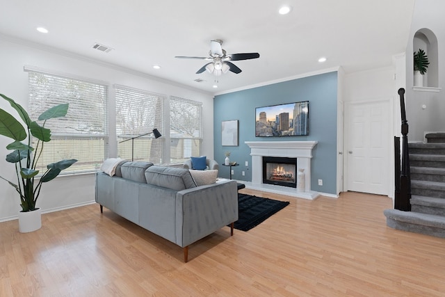 living room featuring light wood-type flooring, visible vents, stairway, and a glass covered fireplace