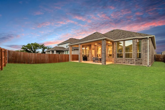 back of property at dusk featuring a patio, a yard, a fenced backyard, and brick siding