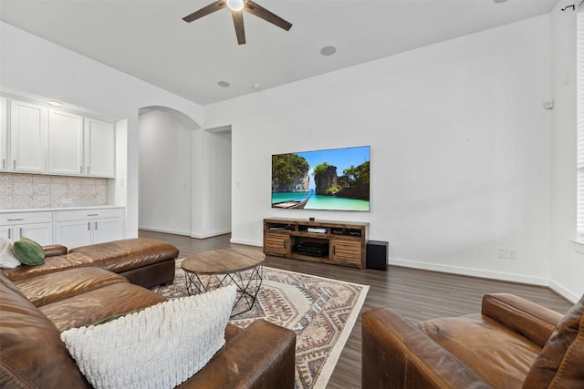 living area featuring arched walkways, wood finished floors, a ceiling fan, and baseboards