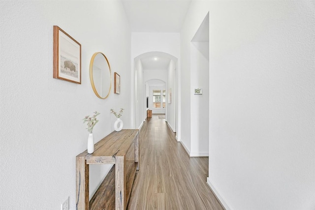 corridor featuring arched walkways, wood finished floors, and baseboards